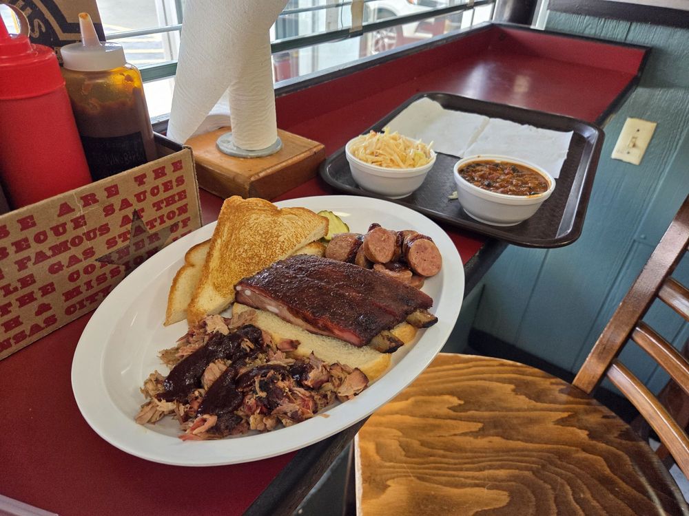 A three meat plate with baked beans.